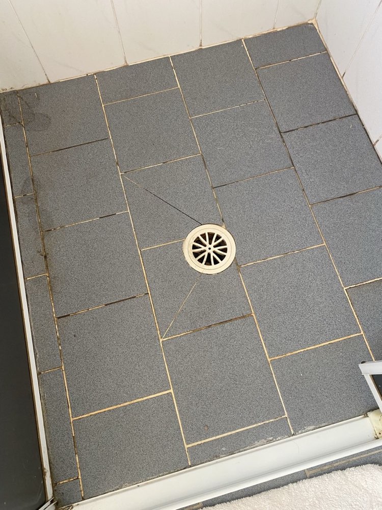Shower floor with worn, discoloured grout — before